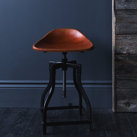 An adjustable bar stool with a brown, tan least saddle-style seat on four metal legs